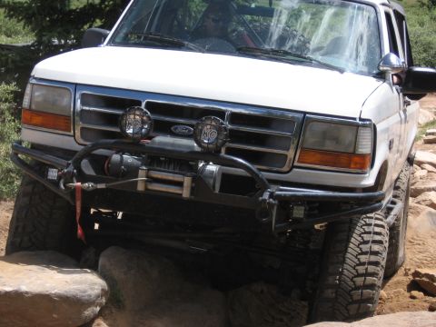 1995 Ford Bronco - 1995 Ford Bronco tackling a challenging off-road trail with large rocks.