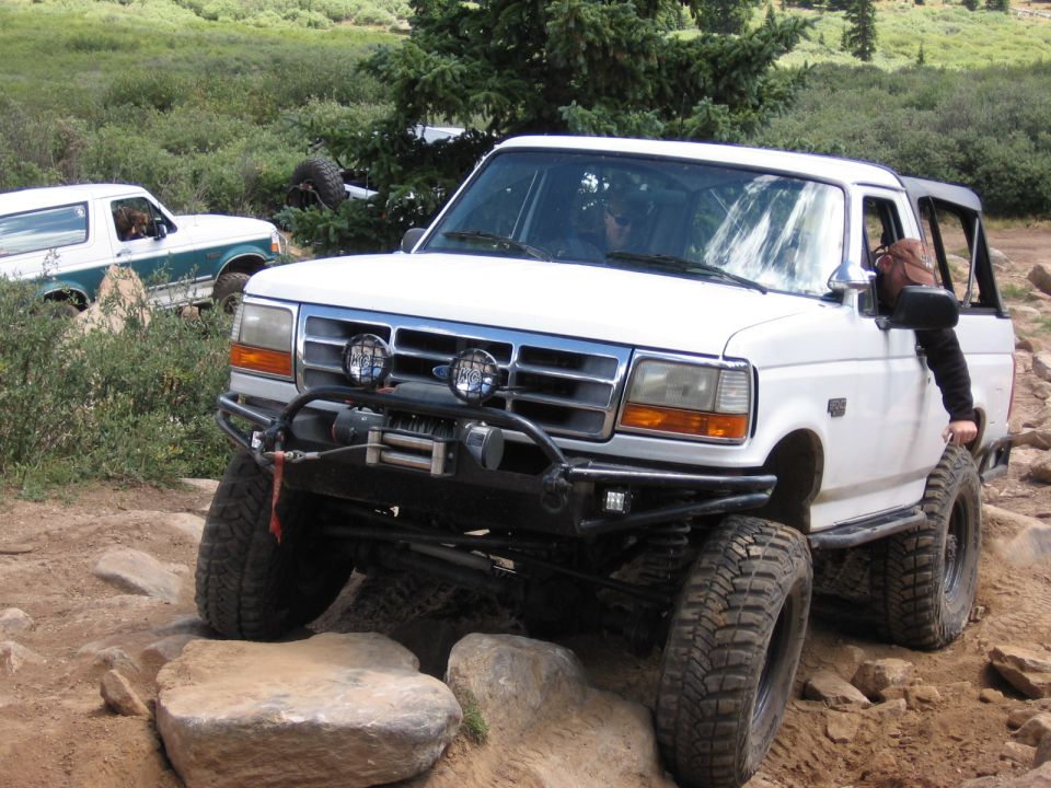White lifted Ford Bronco with winch bumper and KC lights crawling over boulders