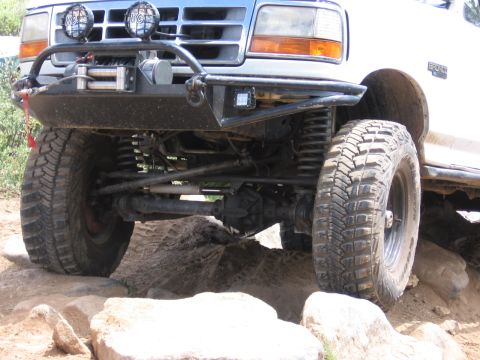 1995 Ford Bronco - White Ford Bronco's front end navigates rocky terrain with its modified bumper and winch.