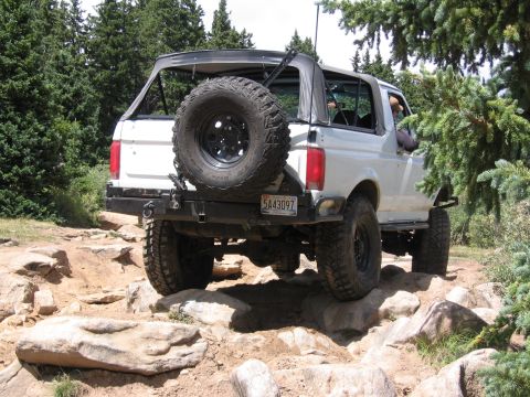 1995 Ford Bronco - A white 1995 Ford Bronco navigates a challenging rocky trail in a wooded area.