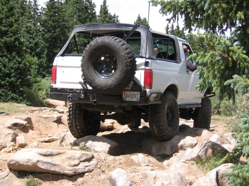 White lifted Ford Bronco flexing over rocks, spare tire on tailgate, soft top folded