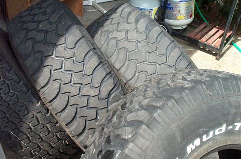 1995 Ford Bronco - Several worn mud-terrain truck tires leaning together outdoors; one sidewall partly legible as mud-T tread tire.