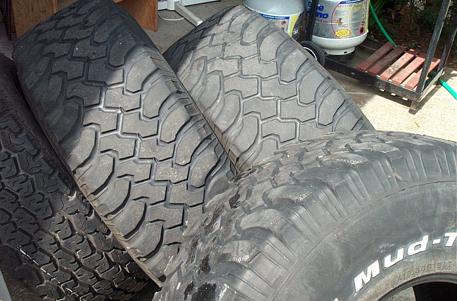 Used off-road mud-terrain truck tires leaning against a wall, one reading mud-T