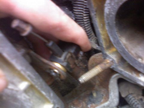 1987 Mercury Grand Marquis - Close-up of a hand adjusting a throttle linkage mechanism on an engine component.