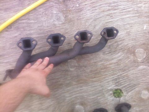 1987 Mercury Grand Marquis - A four-pipe exhaust manifold is shown resting on a weathered wooden surface.
