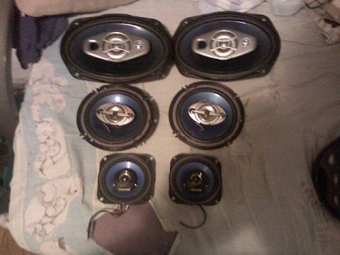 1987 Mercury Grand Marquis - Collection of car speakers, including two oval and two square units, displayed on a patterned surface.