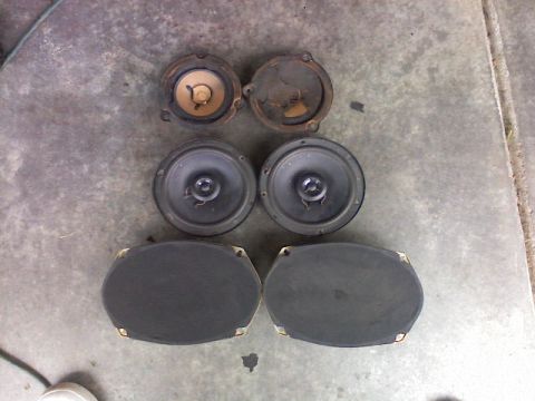 1987 Mercury Grand Marquis - A collection of car speakers, including round and oval types, are displayed on a concrete surface.