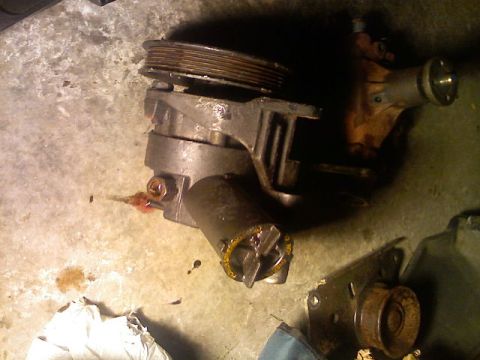 1987 Mercury Grand Marquis - A power steering pump with a pulley and visible fluid leaks sits on a concrete surface.