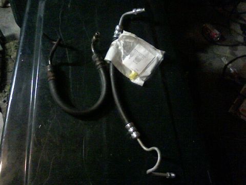 1987 Mercury Grand Marquis - Two automotive hoses are laid out on a dark surface, one still in its original packaging.