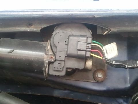 1994 Ford Bronco - A windshield wiper motor mounted in the cowl area, its cylindrical black housing bearing stamped numbers and a gray gearbox cover with a mu…