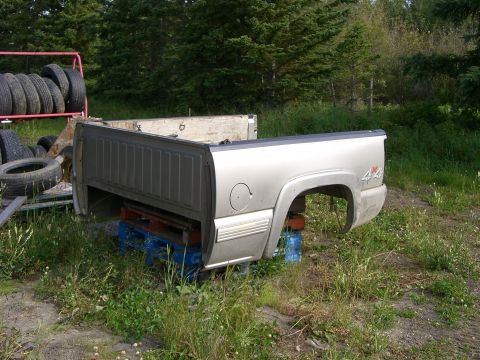 2003 Yamaha GRIZZLY 660 - A silver truck bed is propped up on pallets in a grassy area with trees in the background.