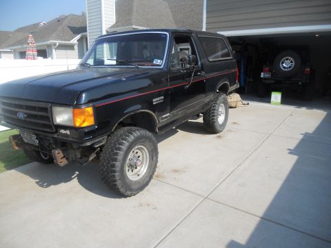 1991 Ford Bronco - A black 1991 Ford Bronco is parked outside a garage, with another vehicle visible inside.
