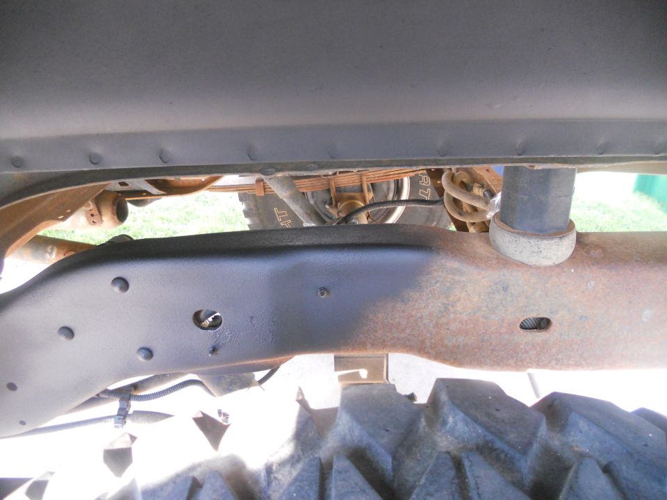 Vehicle frame with rust and black paint, leaf springs, shock absorber, and tire tread visible