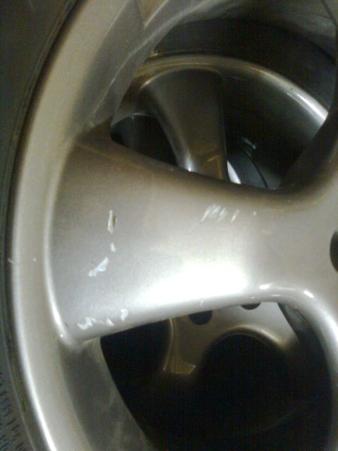 1984 Ford Bronco - Close-up of a damaged silver alloy wheel, showing scuff marks and chips on its surface.