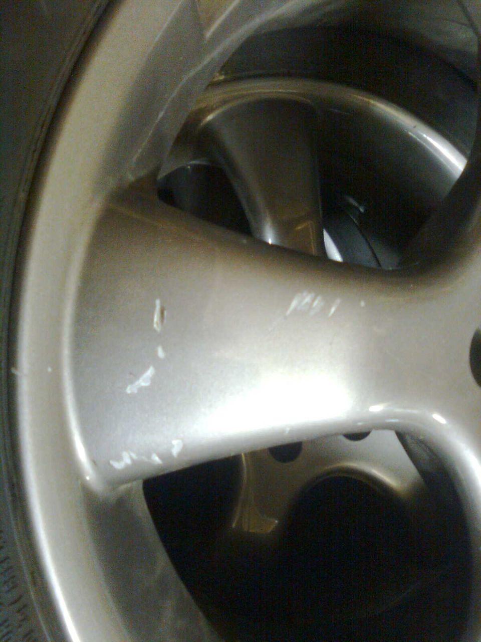 Scratched silver alloy wheel with five spokes and a tire