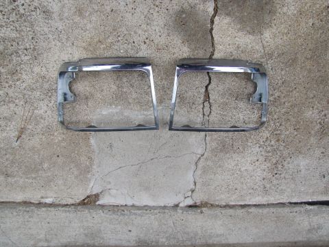 1995 Ford Bronco - Pair of chrome headlight bezels shown on concrete.