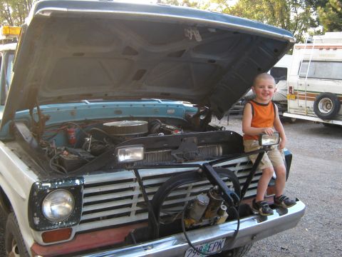 1972 Ford F-250 - A young boy smiles while sitting on the front bumper of a 1972 Ford F-250 with its hood open, revealing the engine bay.