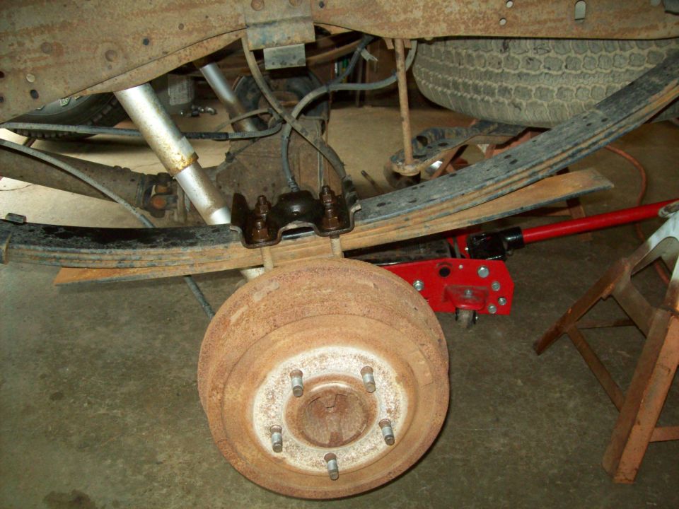 Rear axle with rusty brake drum, leaf spring and U-bolts, wheel removed