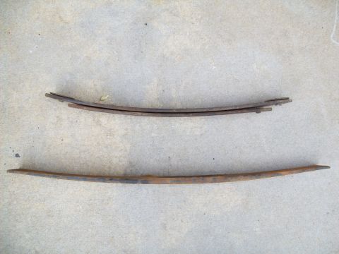 1993 Ford F-150 - Two aged leaf springs lie on a concrete surface, one composed of multiple layers and the other a single piece.