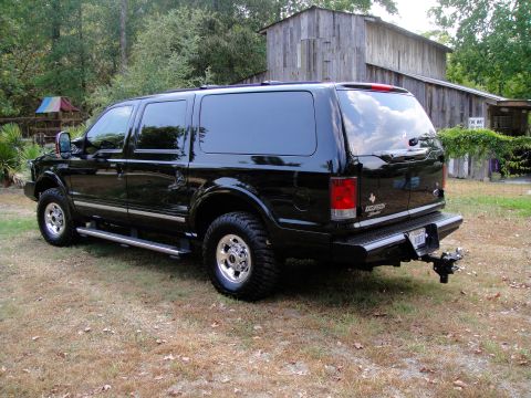2005 Ford Excursion - Rear view of a black Ford Excursion parked on a grassy area with a wooden structure in the background.