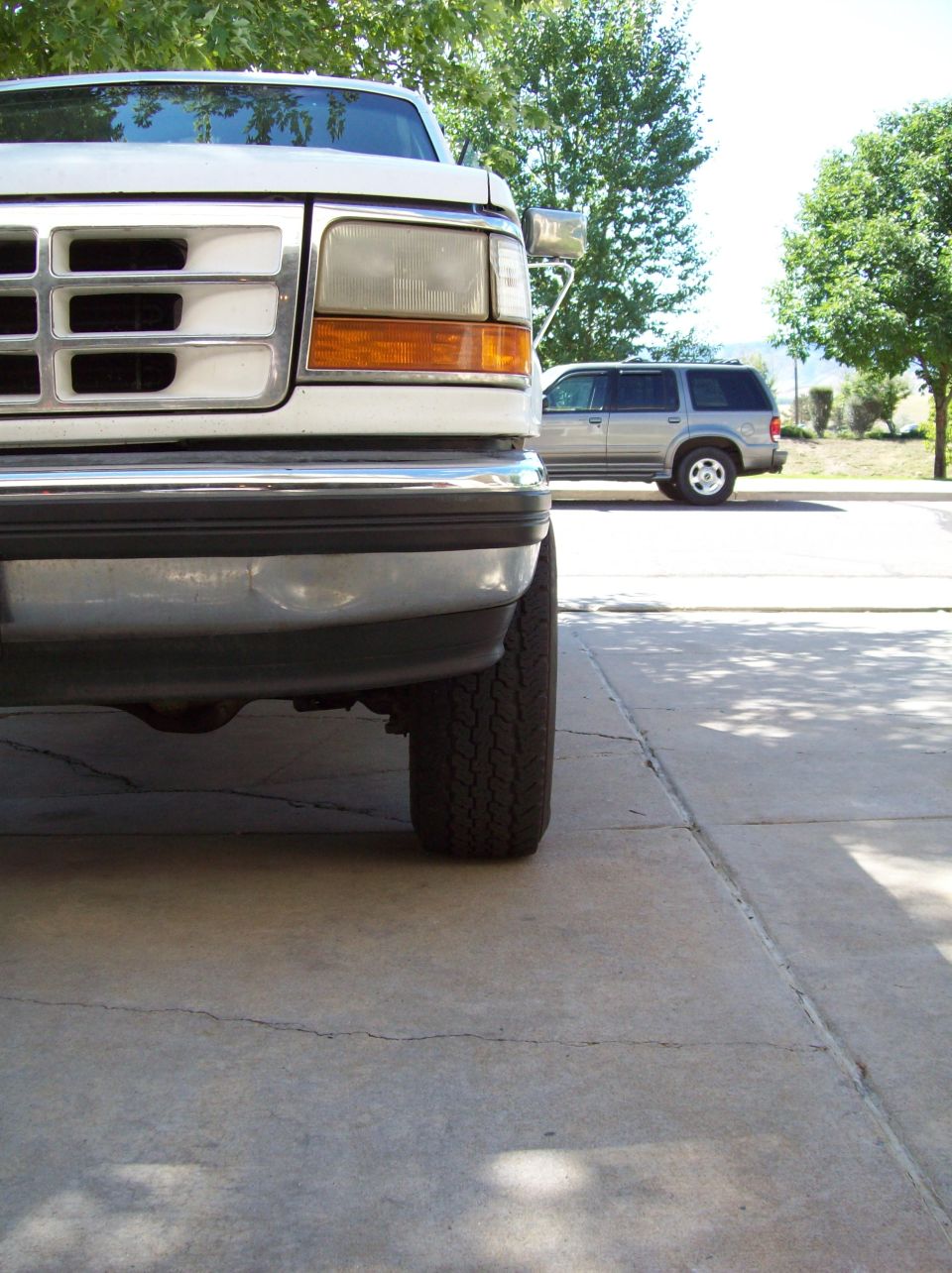 Front corner of a white pickup truck, with a silver SUV in the background
