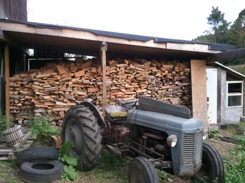 1985 Ford F-150 - A vintage tractor sits outside a shed filled with firewood.