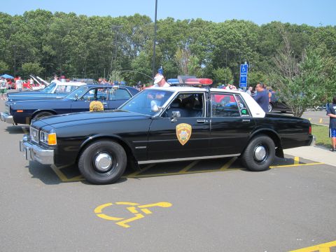 1991 Ford LTD Crown Victoria - black-and-white Highway Patrol sedan with roof light bar parked at an angle in a lot among other classic cars.