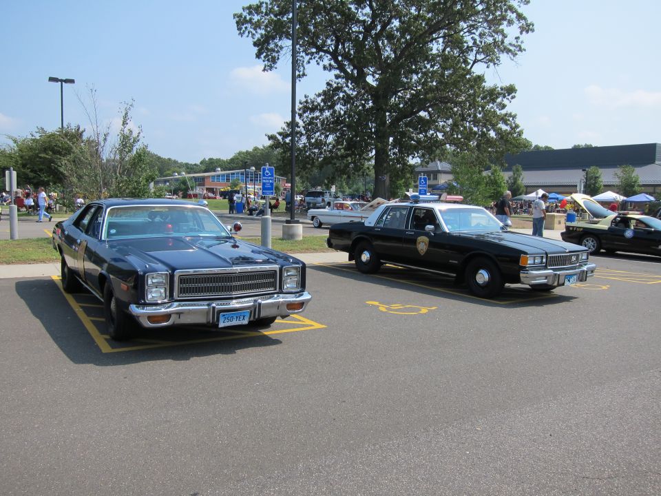 Dark sedan and black-and-white police cruiser parked at outdoor car show