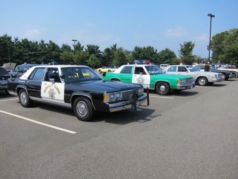 1991 Ford LTD Crown Victoria - black-and-white Highway Patrol sedan with push bar parked beside a green-and-white police car at an outdoor show.
