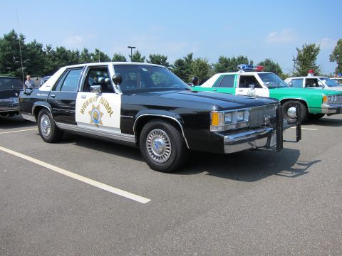 1991 Ford LTD Crown Victoria - Front three-quarter view of a black-and-white Highway Patrol cruiser with star shield and roof lights in a parking lot.