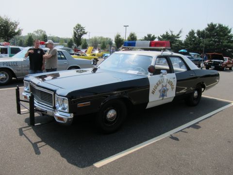 1991 Ford LTD Crown Victoria - black-and-white Highway Patrol cruiser with push bar and roof lights parked in a sunny lot as two men stand nearby.