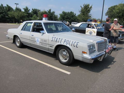 1991 Ford LTD Crown Victoria - silver sedan lettered Rhode Island State Police with a single roof light parked in a lot with people standing nearby.