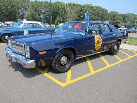1991 Ford LTD Crown Victoria - dark blue police sedan with gold door shield and roof light parked within yellow lines at an outdoor car show.