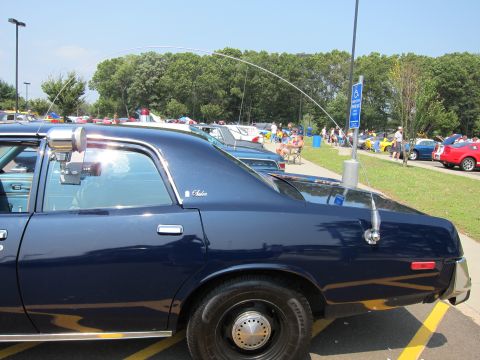 1991 Ford LTD Crown Victoria - Close-up of a dark blue police sedan's rear quarter and roof, with a tall flexible whip antenna and crowded car show behind.