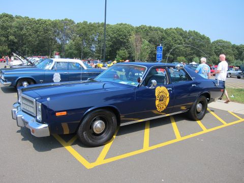 1991 Ford LTD Crown Victoria - dark blue police sedan with a gold Trumbull Police door shield and whip antenna parked at a sunny outdoor car show.