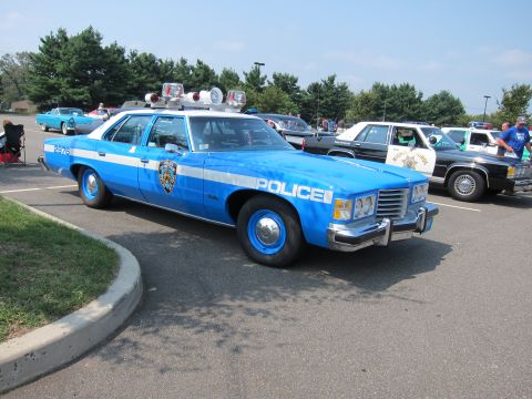 1991 Ford LTD Crown Victoria - blue and white vintage Pontiac police car lettered POLICE sits at a sunny outdoor car show with other classic cars behind it.