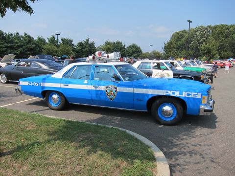 1991 Ford LTD Crown Victoria - blue and white classic Pontiac police sedan marked POLICE and 2976 is parked on grass beside other cars at a show.