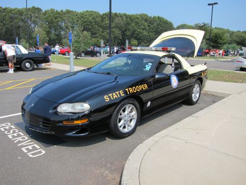 1991 Ford LTD Crown Victoria - black State Trooper Camaro with gold lettering and roof lights is parked in a reserved space at an outdoor car show.