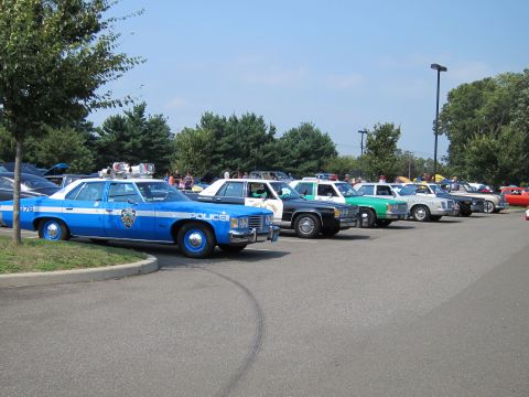 1991 Ford LTD Crown Victoria - line of vintage police cars, led by a blue and white POLICE sedan, parked in a row at an outdoor car show.