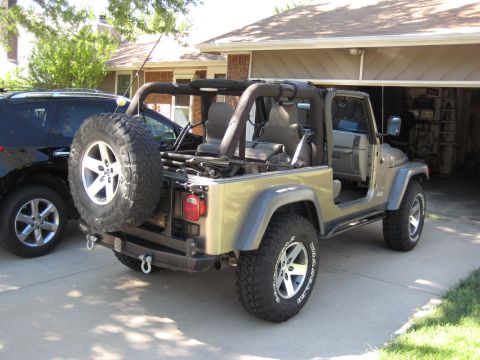 2005 Jeep Wrangler - A tan Jeep Wrangler is parked in a driveway, with a black SUV beside it.