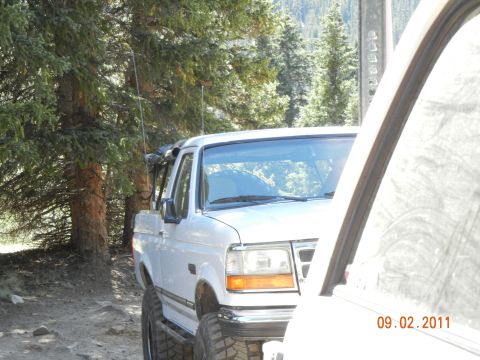 1996 Ford Bronco - A white Ford F-Series truck is parked off-road, partially obscured by another vehicle.
