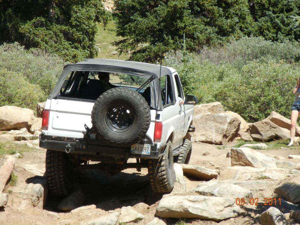 White 1996 Ford Bronco convertible with spare tire on rear, off-roading on rocky terrain