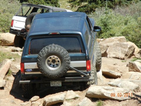 1996 Ford Bronco - Two Ford Broncos off-roading on a rocky trail, one in the foreground and another behind it.