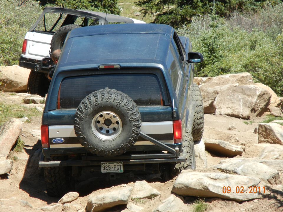 Dark blue Ford Bronco with spare tire on rear, navigating rocky terrain