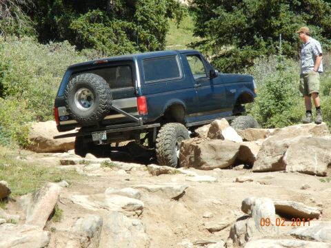 1996 Ford Bronco - A man watches a dark blue Ford Bronco navigate a rocky trail on a sunny day.