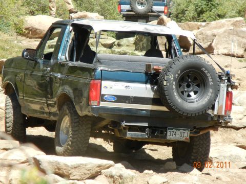 1996 Ford Bronco - A 1996 Ford Bronco navigates a rocky trail, its soft top removed, with another Bronco visible in the background.