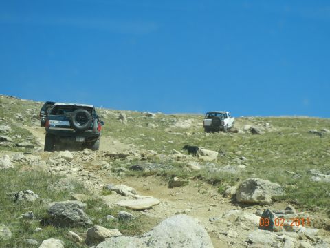 1996 Ford Bronco - Two SUVs navigate a , off-road trail under a clear blue sky.