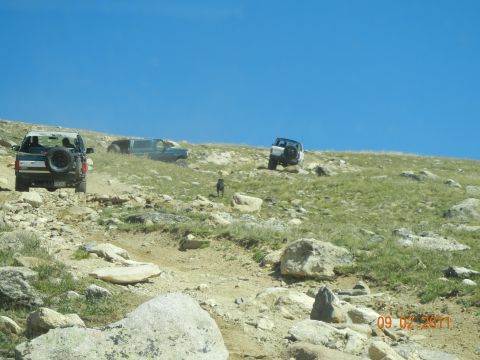 1996 Ford Bronco - Multiple SUVs navigate a challenging off-road trail on a bright, clear day.