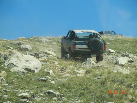 1996 Ford Bronco - Two SUVs navigate a rocky mountain trail under a clear blue sky.
