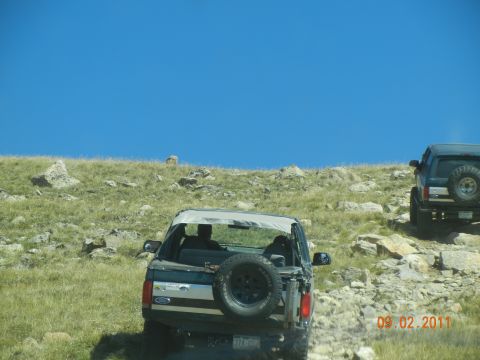 1996 Ford Bronco - Two SUVs, including a 1996 Ford Bronco, navigate a rocky, uphill trail on a sunny day.